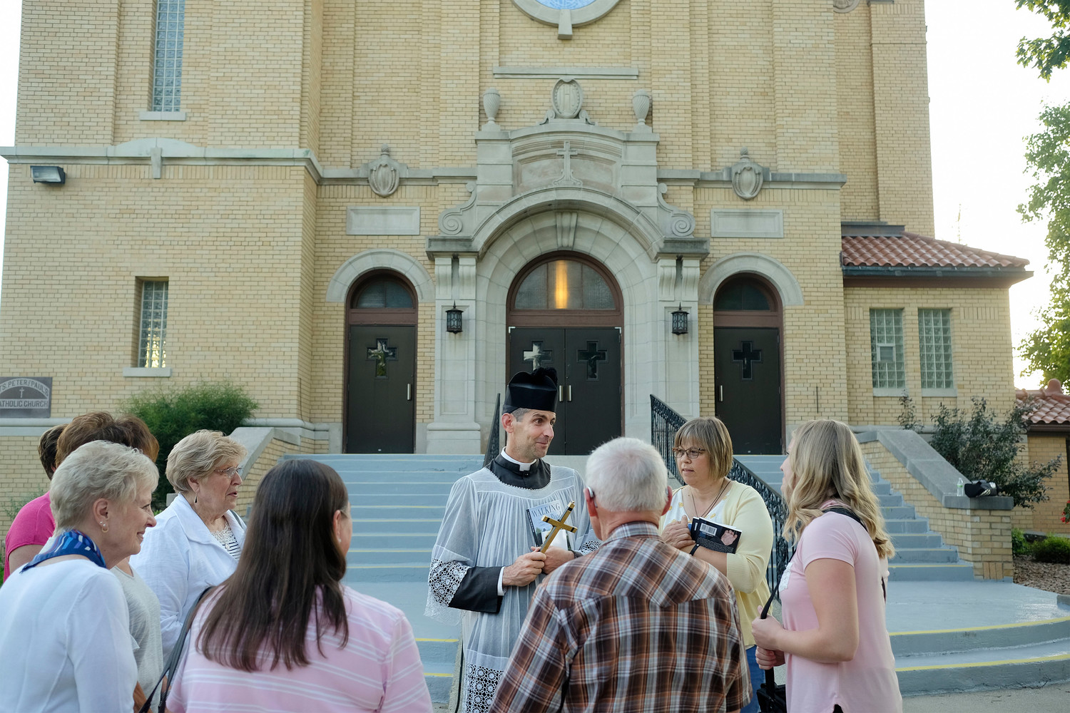 Father Lawrence Carney jokes with people outside Ss. Peter and Paul Church in West Bend, Iowa, July 9. Earlier the “walking priest,” as he is known gave a talk about his street evangelization as part of the parish’s Grotto Speaker Series. A priest of the Diocese of Wichita., Kan, he is on loan to the Diocese of Kansas City-St. Joseph, Mo., where he is chaplain to the Benedictines of Mary, Queen of Apostles in Gower, Missouri.